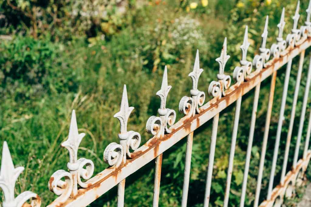 A detailed view of an ornate, rusty fence against a vibrant garden backdrop, showcasing the benefits of native plant gardening.
