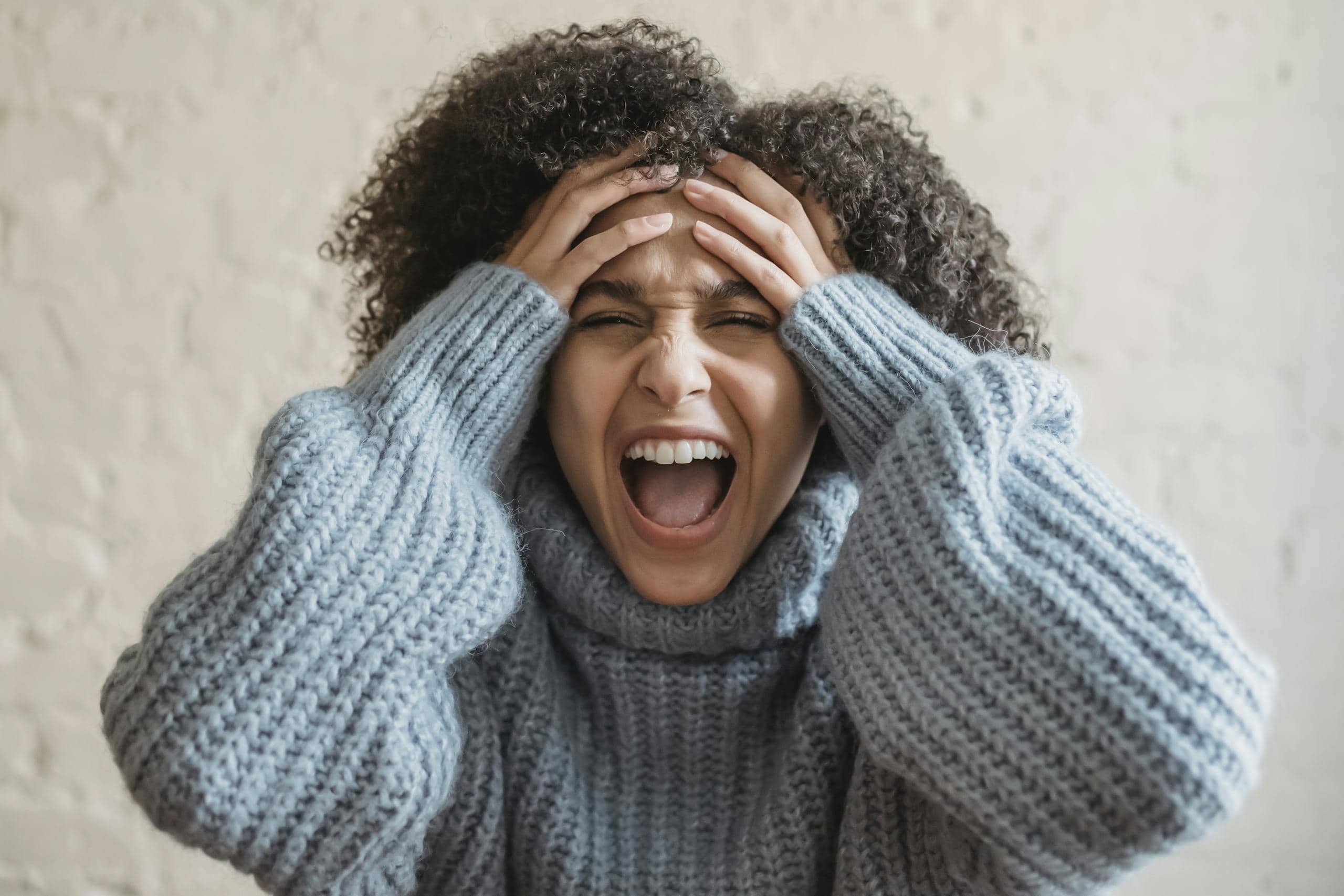 A woman wearing a sweater, expressing frustration with hands on head, too overwhelmed to care about why native gardening matters.