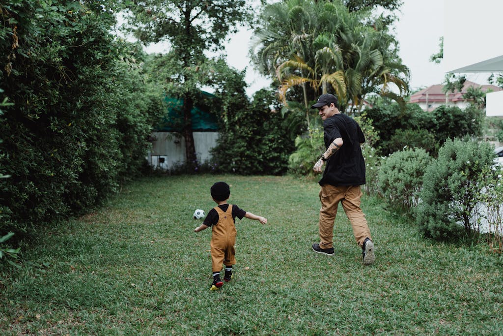 Father and son bonding over a game of football in their lush green garden, enjoying fun family time.