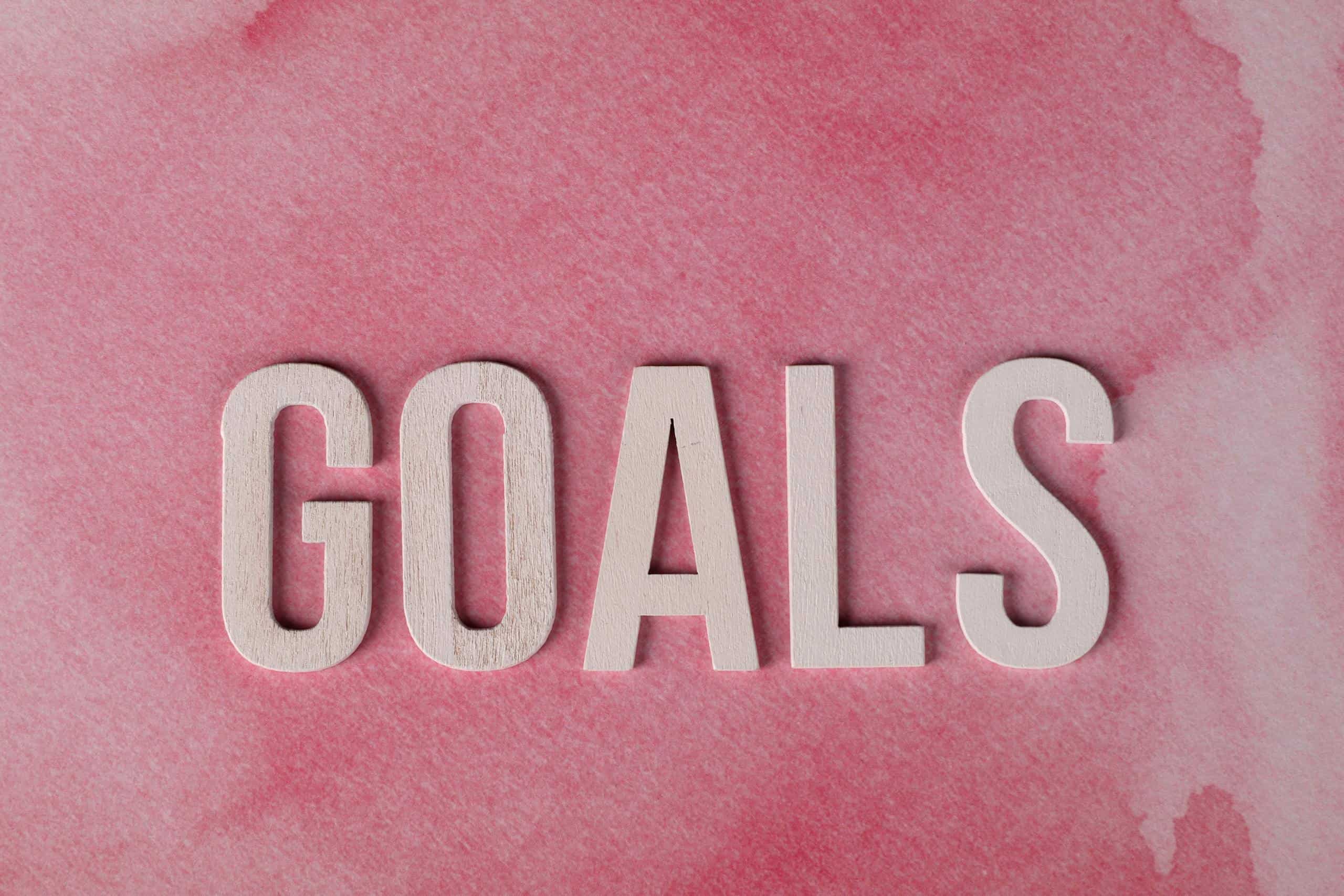 Motivational word 'GOALS' on a pink watercolor background for inspiration about native gardening goals.